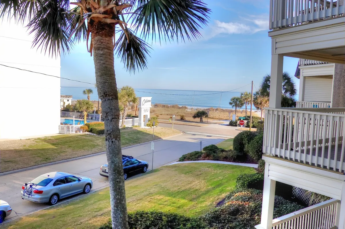 A serene view from a higher vantage point, looking out toward the ocean beyond palm trees and a quiet road. The scene embodies calm and relaxation, emphasizing the proximity to the water and unobstructed ocean views, reminiscent of Myrtle Beach’s Golden Mile.