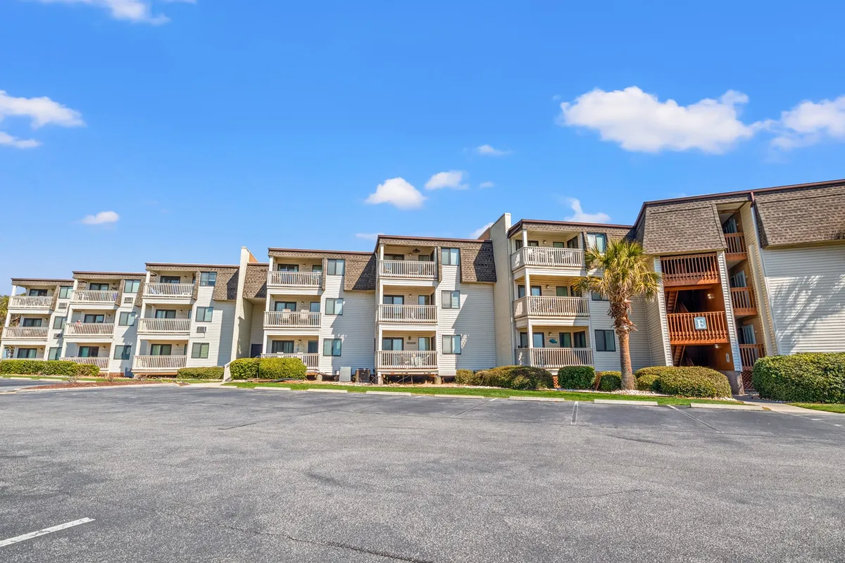 A welcoming exterior shot of the Ocean Forest Villas building with inviting balconies and mature palm trees in the foreground. The image captures the quiet residential vibe, with balconies perfectly poised for relaxing, enjoying morning coffee, or watching the sunset. The general atmosphere is serene and ideal for couples or adult groups seeking a peaceful retreat.