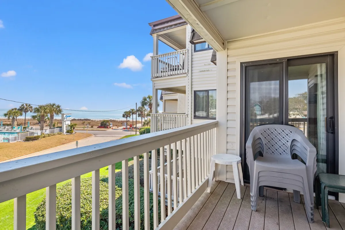 A tranquil exterior scene featuring a private balcony with a sturdy railing and comfortable outdoor seating. The view from the balcony stretches out over a landscape, offering glimpses of the shoreline and ocean in the distance. The setting is beautifully lit with soft natural light, perfect for enjoying a quiet morning coffee or watching the sunset.