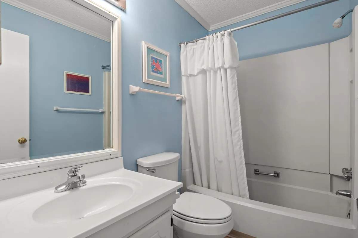 A spacious, well-lit bathroom with a vanity and sink, mirror, bathtub, toilet, and framed artwork on the walls. The decor and fixtures evoke a clean, inviting, and tranquil space for personal grooming and relaxation after a beach day.