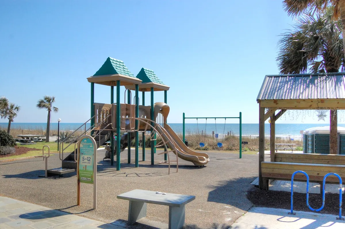 A vibrant playground and picnic area set against the backdrop of the ocean, with swings and family-friendly amenities. Children are playing, and families are enjoying outdoor time together, highlighting joyful, all-ages recreation.