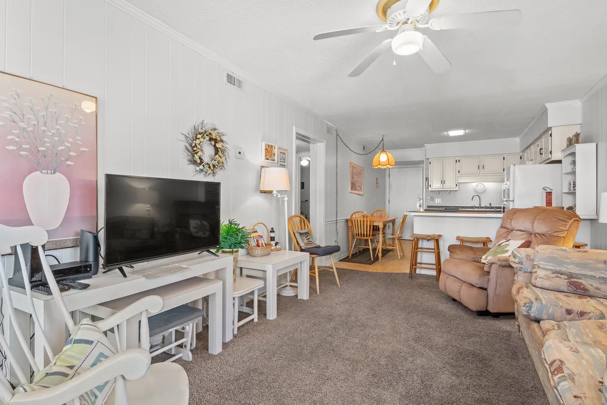 A cozy interior view featuring a TV on a stand, a comfortable couch with colorful cushions, a dining table with chairs, and decorative wall art. The space feels warm and inviting, ideal for both relaxation in the living area and for socializing or sharing meals at the dining table.