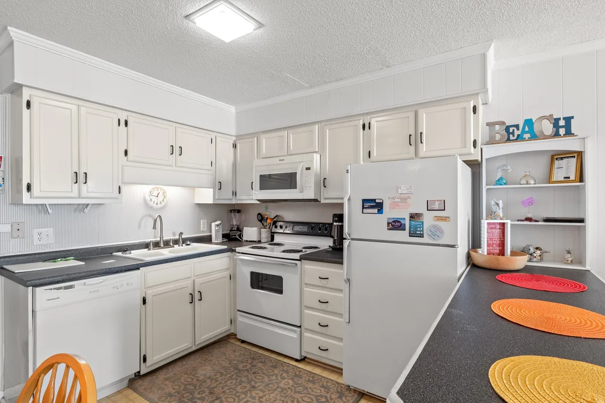 A bright kitchen with cabinets, stainless steel appliances, colorful placemats, and beach-themed decor, creating a cheerful atmosphere for cooking or gathering. The kitchen is fully equipped and welcoming.